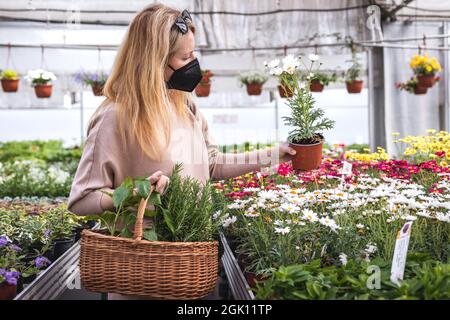 Frau mit FFP2 Gesichtsmaske und Einkaufen von Blumen und Pflanzen im Gartencenter im Frühjahr. Neue normale und Covid-19 Krankheitsvorbeugung beim Einkaufen in Stockfoto