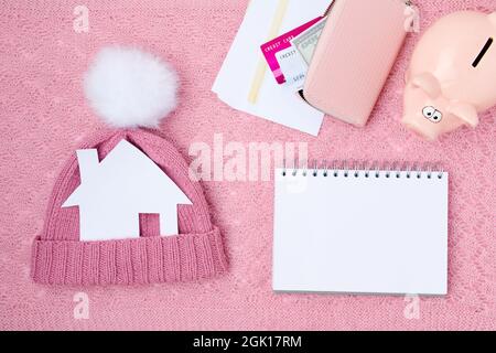 Winter-Wohnung lag mit Sparschwein, Stromrechnungen, Papierhaus, Notebook, Hut, Pompon und Brieftasche auf rosa Hintergrund. Stockfoto