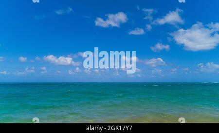 Blick auf den tropischen Ozean auf türkisfarbenes Wasser und blauen Himmel mit geschwollenen Wolken Stockfoto