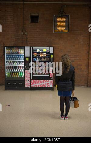 Doncaster, Großbritannien, 22. Mai 2021: An der Abflugtafel werden COVID-Informationen für Bahnreisen angezeigt, die von einer jungen Frau gelesen wurden, die neben Automaten stand Stockfoto