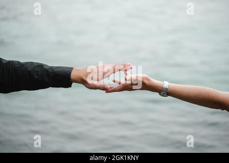 Mann und Frau strechen sich gegenseitig aus und halten die Hände über grauem, monochromen Wasser. Beziehungen, Wiedervereinigung, Liebe, Unterstützung, Verbindungskonzept. Kopieren Stockfoto