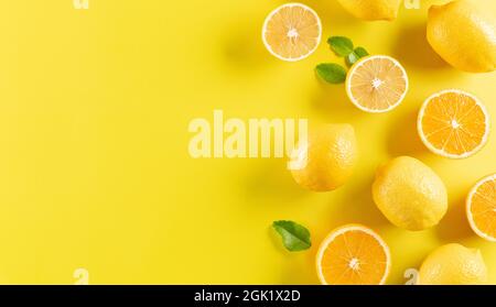 Sommerkomposition aus Orangen, Zitrone und grünen Blättern auf pastellgelbem Hintergrund. Obst minimalistisches Konzept. Stockfoto