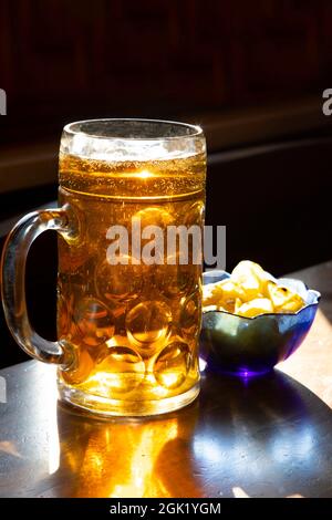 Großer Becher Bier und Chips auf einem Holztisch in einem Pub Stockfoto