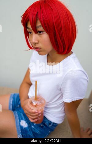 Rote Blutkörperchen Cosplay Schauspielerin sitzend trinken eine Smoothie | asiatische Teenage-Mädchen in roten Perücke Stockfoto