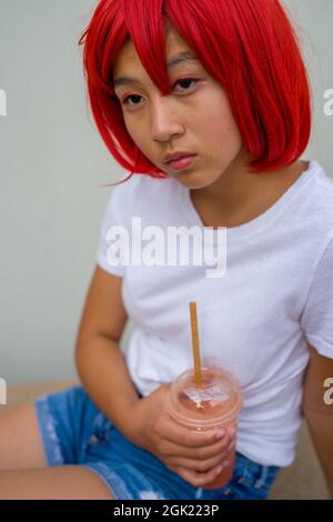 Rote Blutkörperchen Cosplay Schauspielerin sitzend trinken eine Smoothie | asiatische Teenage-Mädchen in roten Perücke Stockfoto