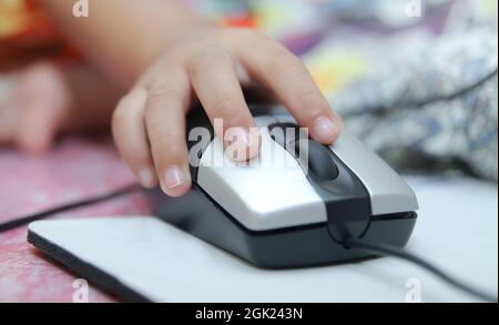 Die Kinderhand hält eine Computermaus oder -Tastatur. Das Kind lernt online und spielt zu Hause am Computer. Schule, Bildung, Technologie. Stockfoto