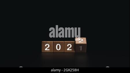 2022 Frohe Neujahrsgrüßen und Frohe Weihnachten Banner. Drehen von Holzwürfelblöcken für den Wechsel des Jahres von 2021 auf 2022 auf dunklem Hintergrund. Stockfoto