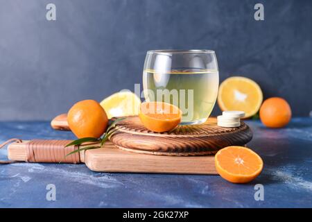 Glas mit leckerem Getränk, Pillen und Zitrusfrüchten auf farbigem Hintergrund Stockfoto