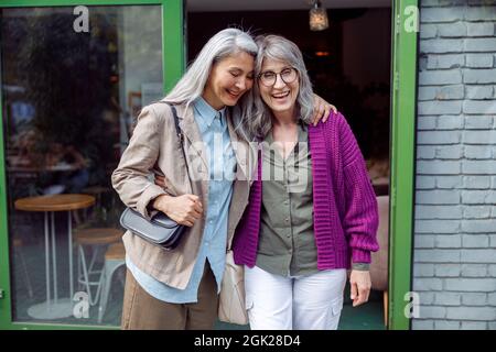 Ziemlich ältere asiatische Dame umarmt Freund in lila Jacke steht in der Nähe Café auf der Straße Stockfoto