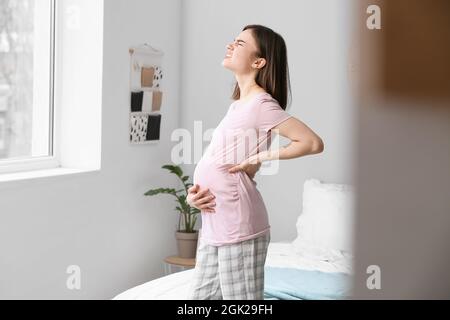 Junge, schwanger gebliebene Frau leidet Rückenschmerzen im Schlafzimmer Stockfoto