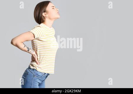 Junge Frau, die unter Rückenschmerzen auf grauem Hintergrund leidet Stockfoto