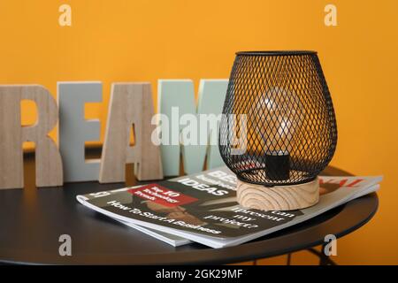 Stilvolle Lampe mit Zeitschriften und Dekor auf dem Tisch neben der Farbwand Stockfoto