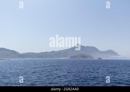 Blick auf einen fernen Berg inmitten des großen blauen Ozeans und einen weichen klaren Himmel Stockfoto