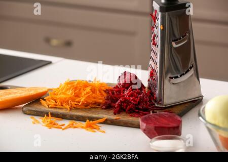 Holzbrett mit geriebener Karotte und Rote Beete auf dem Tisch in der Küche Stockfoto