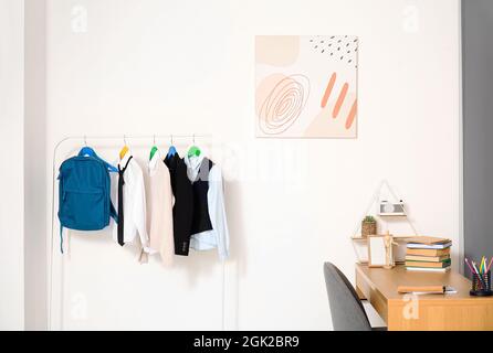 Gestell mit stilvoller Schuluniform und Rucksack im Innenraum Stockfoto