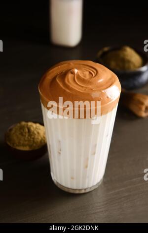 Ein Glas leckeren dalgona hojicha Latte auf dunklem Holzhintergrund Stockfoto