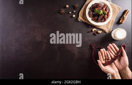 Ramadan Kareem Hintergrund Konzept, Hände halten Rosenkranz Perle mit Datteln Obst und Milch auf dunklem Stein Hintergrund. Stockfoto