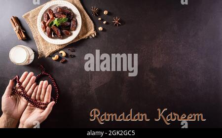 Ramadan Kareem Hintergrund Konzept, Hände halten Rosenkranz Perle mit Datteln Obst und Milch auf dunklem Stein Hintergrund. Stockfoto