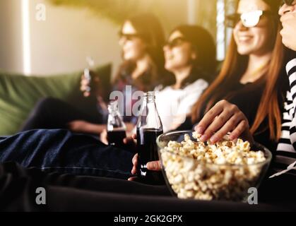 Eine Gruppe von Freunden in 3D-Brillen schaut sich einen Film an, lächelt, lacht. Essen und Trinken, während Sie sich einen Film im Kino ansehen. Mädchen essen Popc Stockfoto