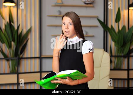 Porträt eines Mädchens in Schuluniform mit einem Buch in der Hand. Das Kind liest ein Lehrbuch. Vorbereitung einer Schülerin auf eine Schulstunde oder Prüfung Stockfoto