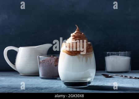 Dalgona kalter Kaffee mit Zutaten und Kopierraum, auf einem dunkelblauen Hintergrund. Süßes koreanisches Getränk Stockfoto