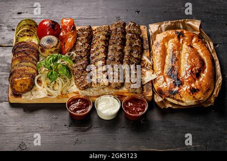 Verschiedene Kebabs aus verschiedenen Fleischsorten. Kalbfleisch, Huhn, Lammkebabs mit Gemüse und Saucen auf einem Holzbrett. Traditionelles türkisches Street Food Stockfoto