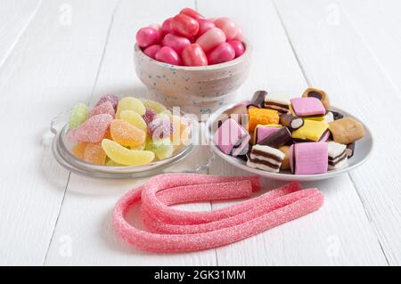 Kaugummis, Süßholzbonbons, Fruchtgummi in Schalen auf weißem Holzhintergrund. Urlaubskonzept, Baby-Leckereien. Ungesunde Lebensmittel. Stockfoto