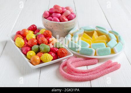 Bunte, kauen Süßigkeiten, Fruchtgummi in Schalen auf weißem Holzhintergrund. Urlaubskonzept, Baby-Leckereien. Ungesunde Lebensmittel. Stockfoto