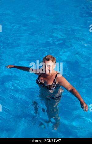 Die Frau steht im Wasser. Blonde mit nassem Haar im schönen Badeanzug steht im Pool und schaut in die Kamera Stockfoto