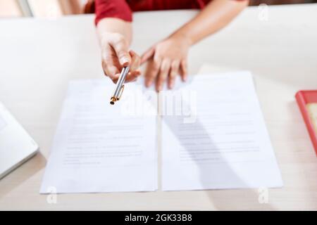 Hände einer Unternehmerin, die dem Geschäftspartner Stift gibt und bittet, ihn zu unterschreiben Stockfoto