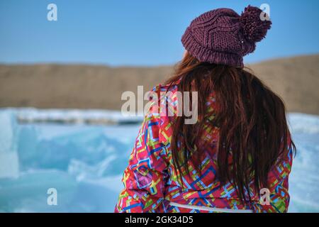 Eine Frau mit langen Haaren in Winterskikleidung wird mit dem Rücken gedreht und schaut irgendwo in die Ferne Stockfoto