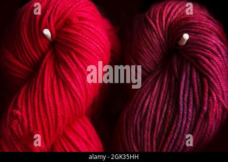 Zwei rote Garnknäuel im Laden. Hintergrund der verschiedenen Wollfäden zum Stricken. Farbe und Textur. Weibliches Hobby Stockfoto