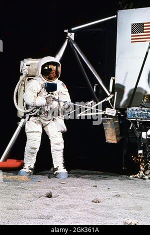 (22. April 1969) --- Astronaut Neil A. Armstrong, der eine Extravehicular Mobility Unit (EMU) trägt, nimmt an einer Simulation des Einsatzes und der Verwendung von Mondwerkzeugen auf der Oberfläche des Mondes Teil, während einer Trainingsübung in Gebäude 9 am 22. April 1969. Armstrong ist der Kommandant der Mondlandemission Apollo 11. Er verwendet einen Messlöffel, um die Probe in den Beutel zu legen. Auf der rechten Seite befindet sich ein Modell der Mondlandefähre (LM) Stockfoto