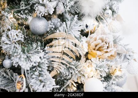 Weihnachtsschmuck in Form einer Rose, eines Farnblattes und Kugeln hängen an einem silbernen Weihnachtsbaum. Weihnachtshintergrund für den Kopierbereich Stockfoto