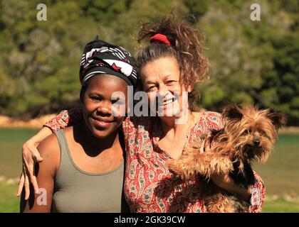 Ältere Dame mit langen Haaren hält ihren Yorkshire Terrier und ihr Freund, das junge schwarze Mädchen Stockfoto