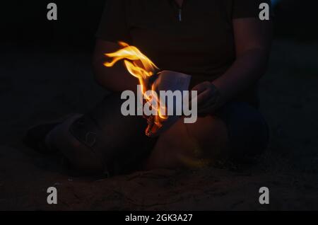 Eine Frau hält ein brennendes Stück Papier in ihrer Hand. Ein gewachsener woma Stockfoto