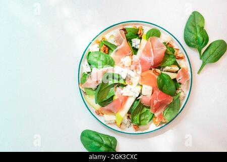 Birnensalat mit Prosciutto, Blauschimmelkäse, Spinat, Walnüssen auf weißem Hintergrund, Draufsicht, Kopierraum Stockfoto
