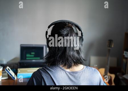 Ein Mann mit langen Haaren, der Kopfhörer trägt und vor einem Laptop sitzt. Musiker, der von zu Hause aus arbeitet. Stockfoto