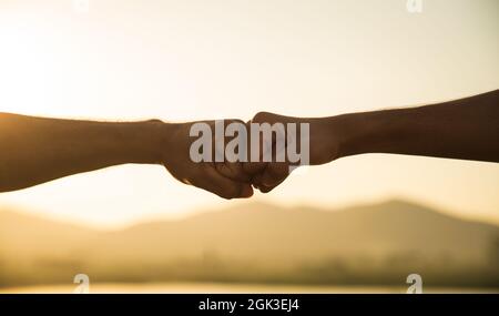 Zwei Mann Hand geben Faust Beule vor dem Berg während des Sonnenuntergangs. Glück, Erfolg, Freundschaft und Gemeinschaftskonzepte. Stockfoto