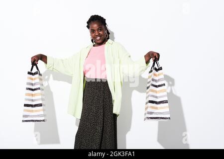 Porträt einer jungen afrikanischen Frau, die Einkaufstaschen in der Hand hält und die Kamera isoliert auf weißem Hintergrund anlächelt Stockfoto