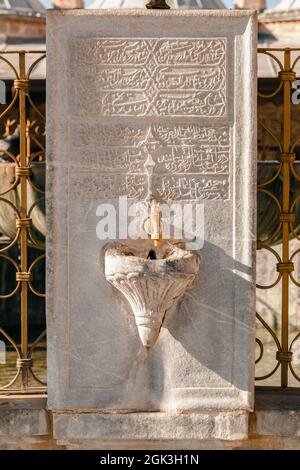 Nahaufnahme eines Wasserhahns auf einem großen alten Marmorstein mit eingravierten alten arabischen Schriften im Mausoleum von Mevlana in Konya, Türkei. Stockfoto