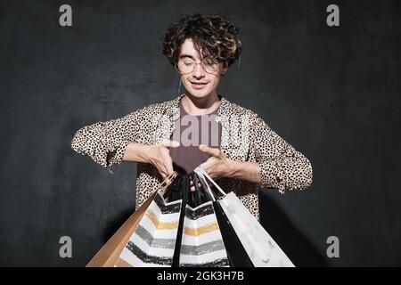 Der junge Modedesigner hält Einkaufstaschen in den Händen vor dem schwarzen Hintergrund Stockfoto