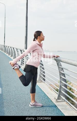 Junge Frau in Sportkleidung, die auf der Brücke steht und Sport macht und auf das schöne Meer blickt Stockfoto
