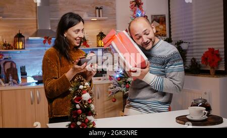 Mann und Frau schenken einander zu weihnachten Geschenkschachteln und feiern Weihnachtsfestlichkeiten. Paare fühlen sich festlich, während sie Geschenke austauschen, die mit rotem Band und Geschenkpapier verziert sind Stockfoto