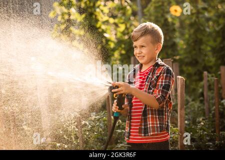 Der kleine Junge wäscht die Pflanzen und macht große Wasserspritzer Stockfoto