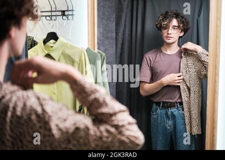 Junger Mann, der in der Umkleide vor dem Spiegel steht und sich ein neues Hemd anprobiert Stockfoto