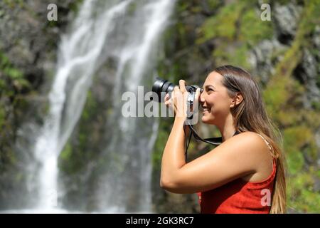 Seitenansicht Porträt einer glücklichen Frau, die Fotos mit spiegelloser Kamera in der Natur macht Stockfoto