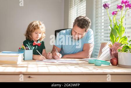 Bärtiger Vater schreibt Schulaufgaben mit seinem Jungen Sohn im Klassenzimmer, Hausaufgaben Stockfoto