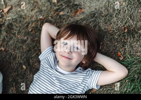 Kind liegt auf dem Rücken im Gras im Park. Junge chillen auf grünem Rasen. Kind entspannt sich draußen und ruht seinen Kopf auf der Gartenwiese Stockfoto