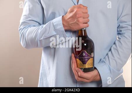 Riga, Lettland, 4. August 2021: Hände eines jungen Mannes, der eine Flasche Courvoisier VSOP Cognac auf hellgrauem Hintergrund hält Stockfoto